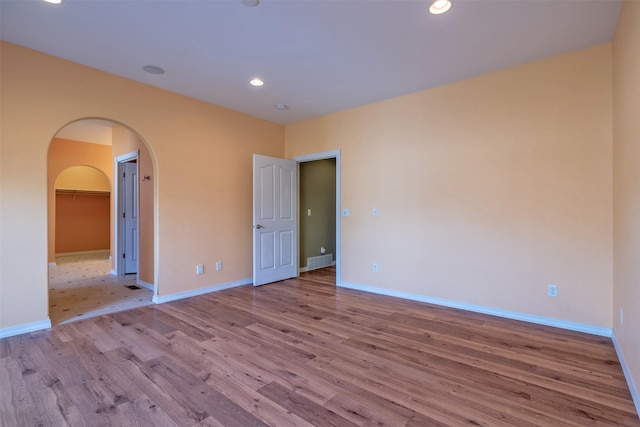 unfurnished room with baseboards, arched walkways, and light wood-style flooring