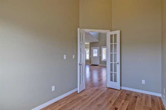 unfurnished room with baseboards, french doors, a towering ceiling, and light wood-style flooring