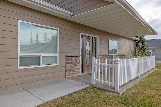 property entrance with stone siding, a lawn, fence, and a patio