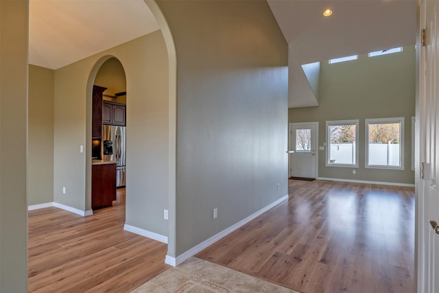 spare room featuring recessed lighting, arched walkways, light wood-style floors, baseboards, and high vaulted ceiling