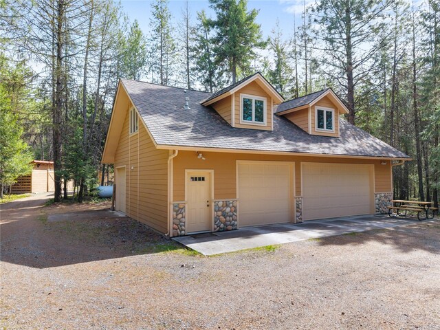 69 Fir Dr, Thompson Falls, MT 59873 - view of front of home with roof with shingles, stone siding, a detached garage, and driveway