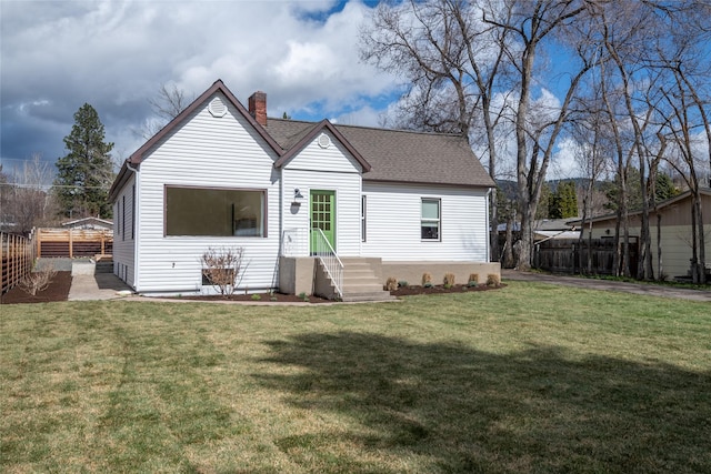 back of property with a yard, a chimney, fence, and roof with shingles