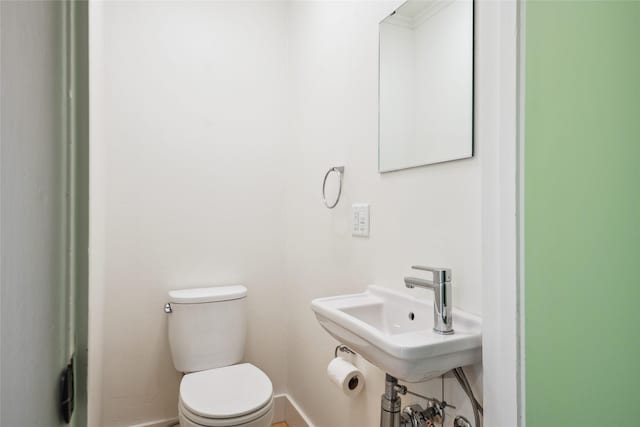 half bathroom with a sink, toilet, and baseboards