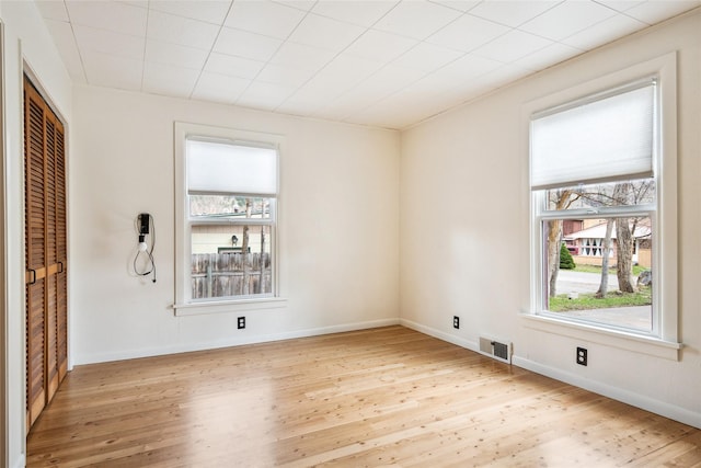 empty room with wood finished floors, baseboards, and visible vents