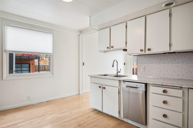 kitchen with light countertops, white cabinetry, light wood finished floors, dishwasher, and a sink