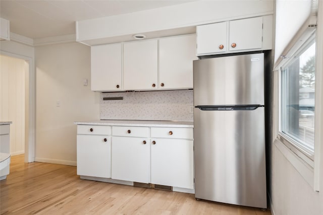 kitchen featuring light countertops, light wood-type flooring, freestanding refrigerator, white cabinetry, and backsplash