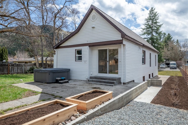 back of property with entry steps, fence, a hot tub, and a vegetable garden