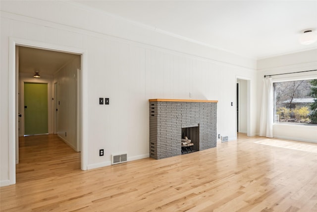 unfurnished living room with ornamental molding, visible vents, wood finished floors, a brick fireplace, and baseboards