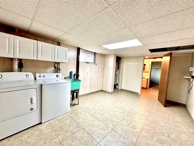 laundry room with baseboards, wooden walls, cabinet space, washer and dryer, and a sink
