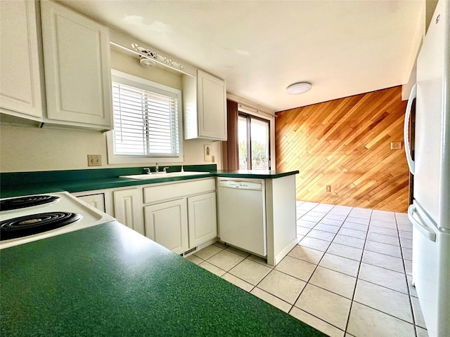 kitchen featuring light tile patterned floors, a sink, dark countertops, white appliances, and wooden walls