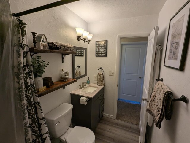 bathroom with toilet, a textured wall, a textured ceiling, vanity, and wood finished floors