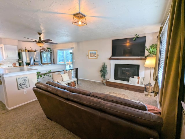 living room featuring a ceiling fan, baseboards, a glass covered fireplace, and carpet