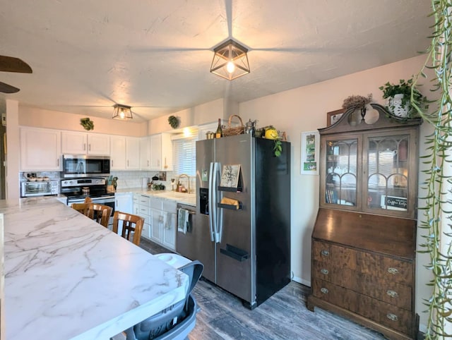kitchen with dark wood finished floors, white cabinets, appliances with stainless steel finishes, a sink, and backsplash