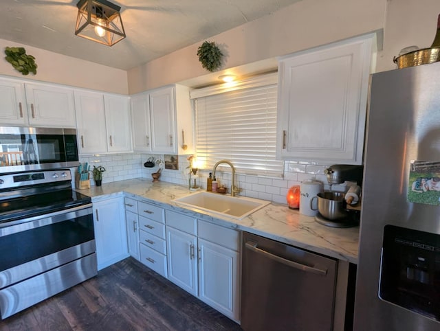 kitchen with dark wood-type flooring, white cabinets, appliances with stainless steel finishes, a sink, and decorative backsplash