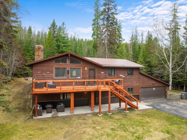 back of house with a wooded view, stairway, a wooden deck, a garage, and a lawn