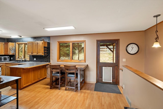 kitchen featuring light wood-style flooring, brown cabinetry, pendant lighting, and a sink