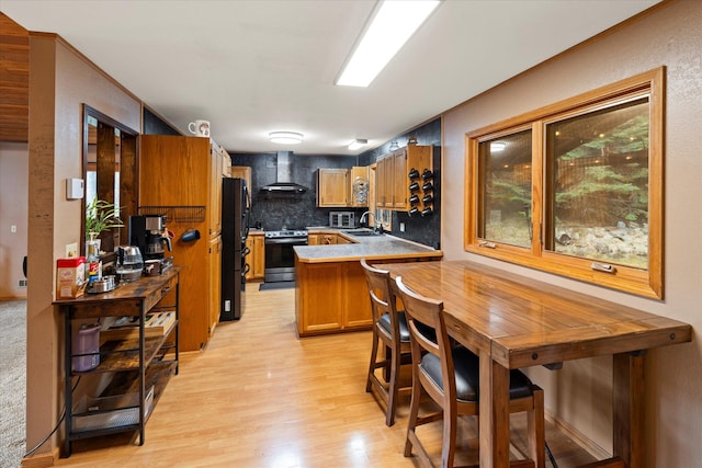 kitchen featuring stainless steel range with electric stovetop, a sink, wall chimney range hood, freestanding refrigerator, and light wood-style flooring