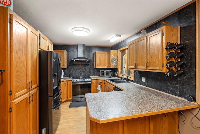 kitchen with wall chimney exhaust hood, light wood-style flooring, a peninsula, appliances with stainless steel finishes, and a sink