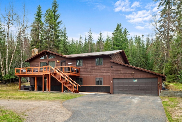 cabin featuring a wooded view, a garage, a chimney, stairway, and driveway