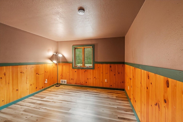 bonus room with visible vents, a textured ceiling, a wainscoted wall, and wood finished floors