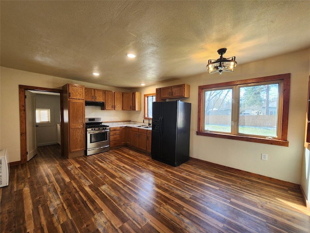 105 Stapp Ln, Darby, MT 59829 - kitchen featuring stainless steel gas range oven, black refrigerator with ice dispenser, dark wood-style floors, and under cabinet range hood