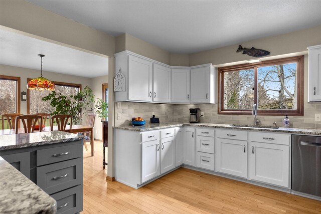 kitchen featuring light wood-type flooring, backsplash, light stone countertops, dishwasher, and a sink