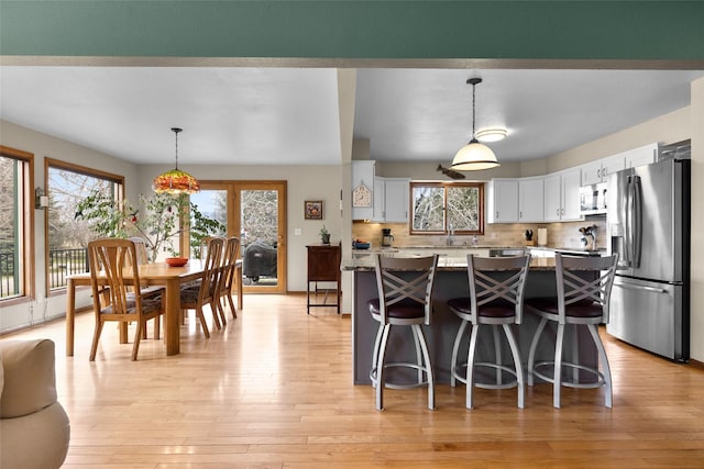 kitchen with stainless steel fridge with ice dispenser, a wealth of natural light, light wood-style flooring, and white cabinets