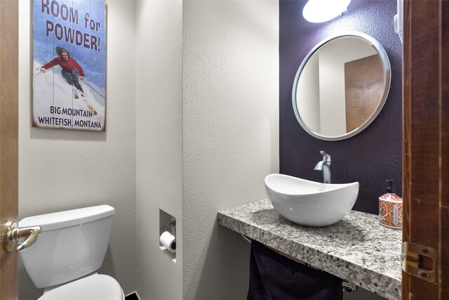 half bathroom featuring toilet, vanity, and a textured wall