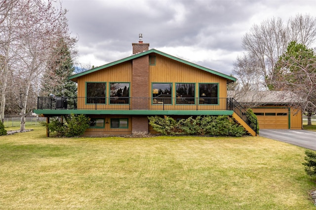 back of house featuring an outbuilding, driveway, a chimney, and a lawn