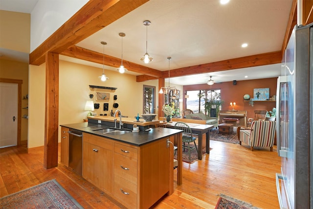 kitchen with a sink, dark countertops, beam ceiling, stainless steel appliances, and light wood-style flooring