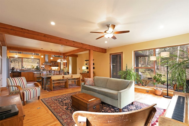 living room featuring light wood-style flooring, a healthy amount of sunlight, ceiling fan with notable chandelier, and beam ceiling
