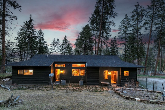 back of house at dusk with a shingled roof