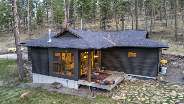 back of house with a wooded view and roof with shingles