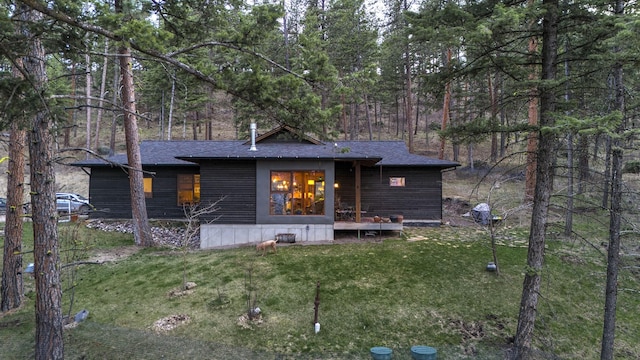 back of property featuring roof with shingles, a wooded view, and a lawn