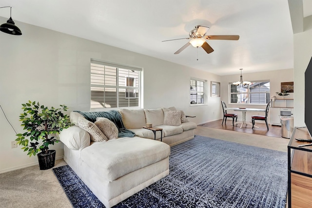 living area featuring ceiling fan with notable chandelier and baseboards