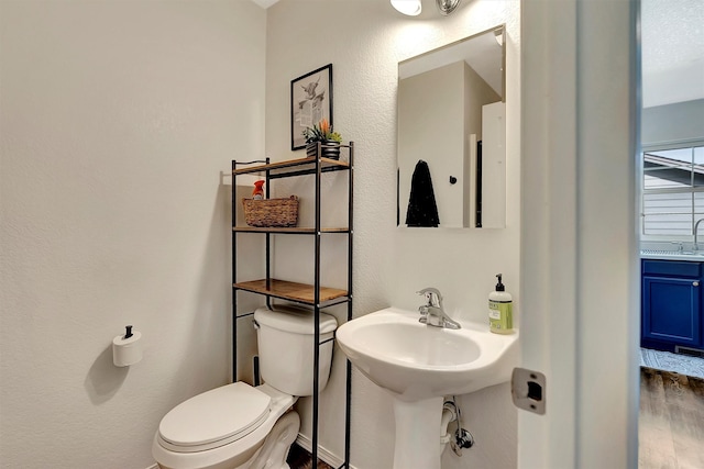 half bathroom with a sink, a textured wall, toilet, and wood finished floors