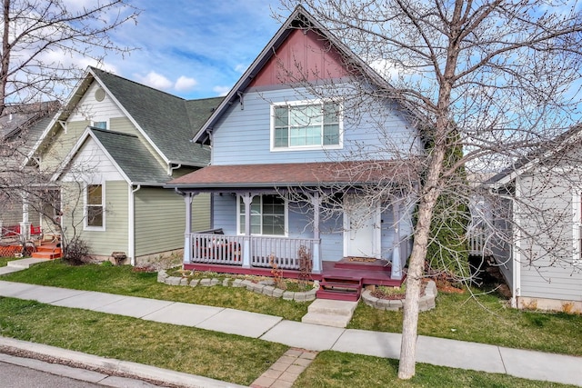 view of front of home with a shingled roof, covered porch, and a front lawn