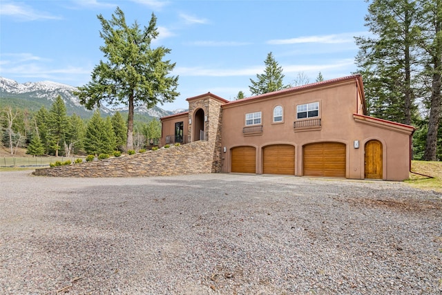 1636 Lake Blaine Rd, Kalispell, MT 59901 - mediterranean / spanish house featuring an attached garage, stucco siding, a mountain view, and gravel driveway