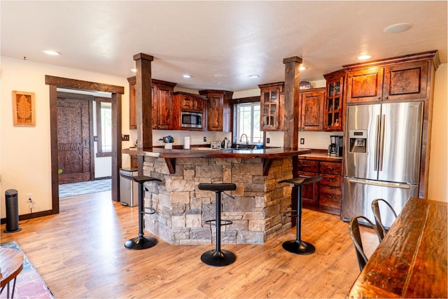 kitchen with a kitchen bar, light wood-style floors, glass insert cabinets, and stainless steel appliances