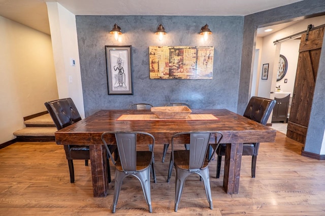 dining room with a barn door, an accent wall, baseboards, and wood finished floors