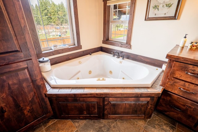 full bath with a whirlpool tub and stone finish flooring