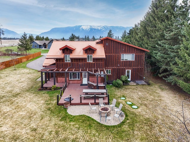 rear view of house with a yard, a patio, a deck with mountain view, metal roof, and a fire pit