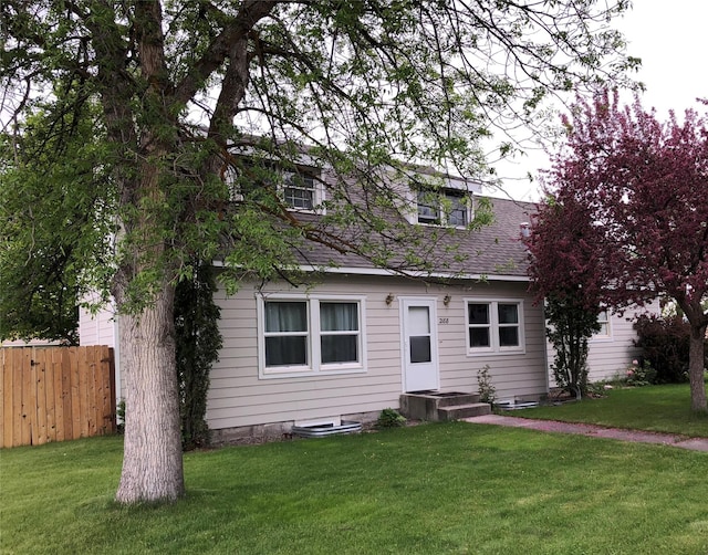 cape cod house featuring roof with shingles, a front yard, and fence