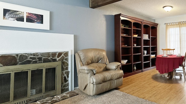 living area with a stone fireplace, wood finished floors, and a textured ceiling