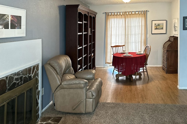 dining space with a textured ceiling, a stone fireplace, baseboards, and wood finished floors