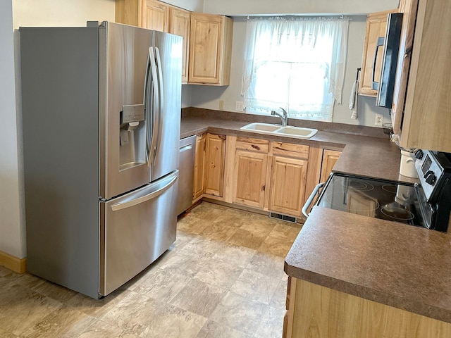 kitchen with light brown cabinets, dark countertops, visible vents, stainless steel appliances, and a sink