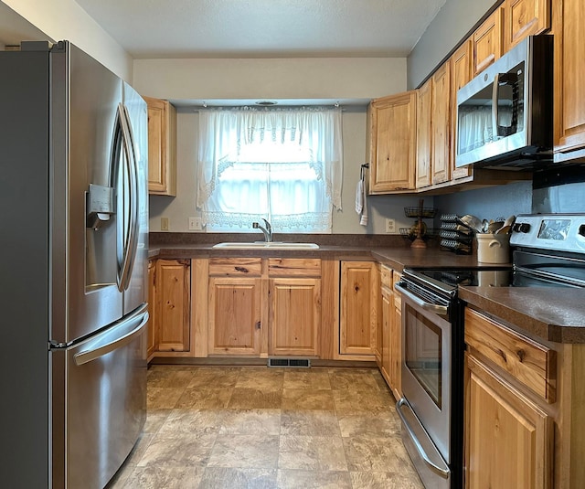 kitchen with dark countertops, visible vents, appliances with stainless steel finishes, stone finish flooring, and a sink