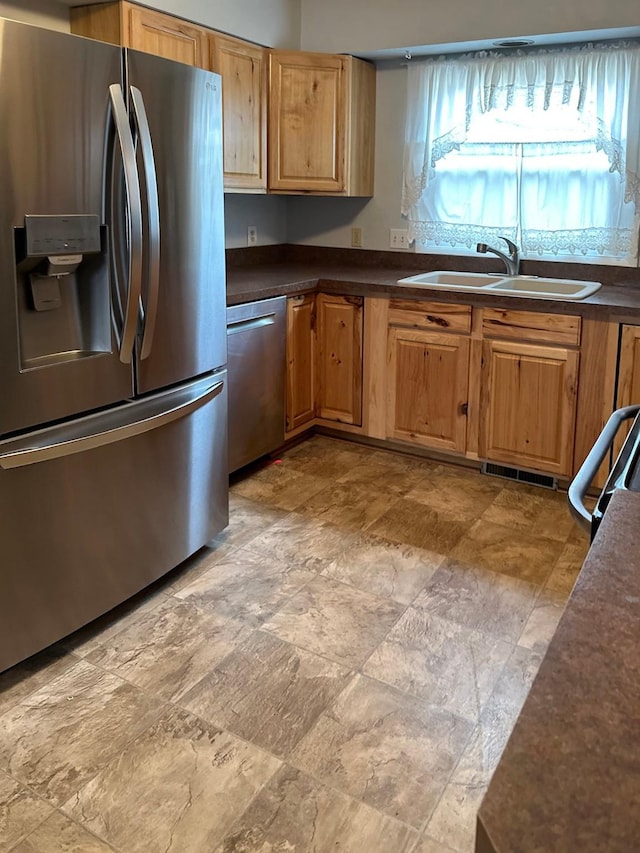 kitchen with appliances with stainless steel finishes, stone finish floor, a sink, and dark countertops