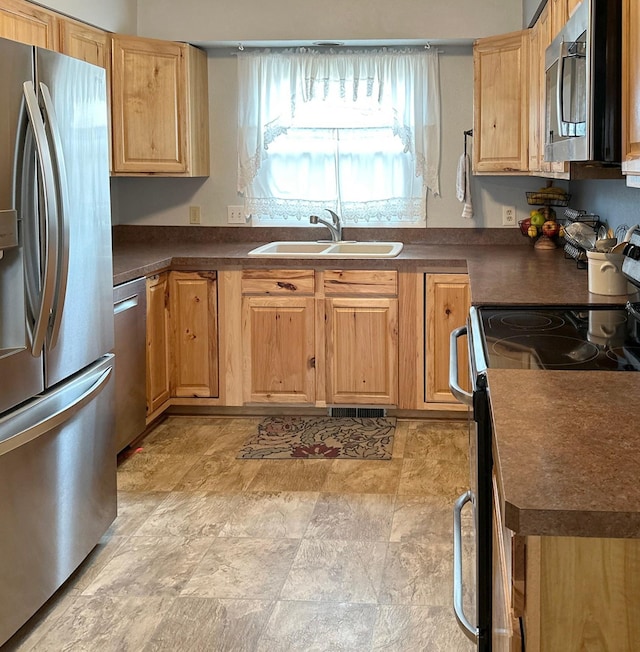 kitchen with light brown cabinetry, appliances with stainless steel finishes, a sink, and dark countertops