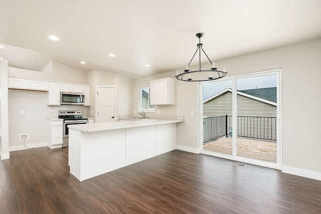 kitchen with a peninsula, appliances with stainless steel finishes, dark wood-style flooring, a sink, and light countertops